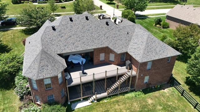 Aerial view of a large brick house with a spacious deck and landscaped yard.
