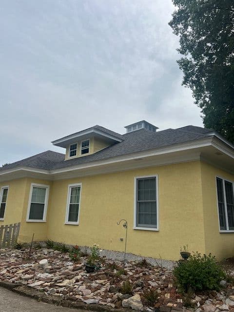 Yellow house with a grey roof, decorative windows, and a landscaped garden.