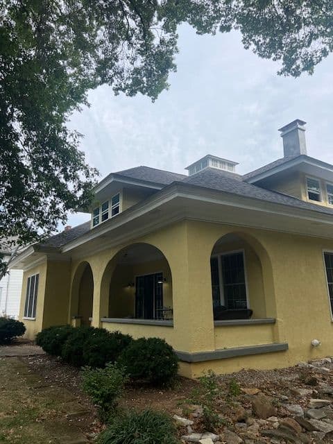 Yellow house with arched porch and lush landscaping under a cloudy sky.