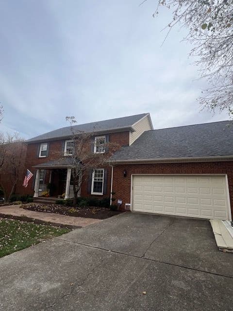 Two-story brick house with an American flag, landscaped yard, and a garage.