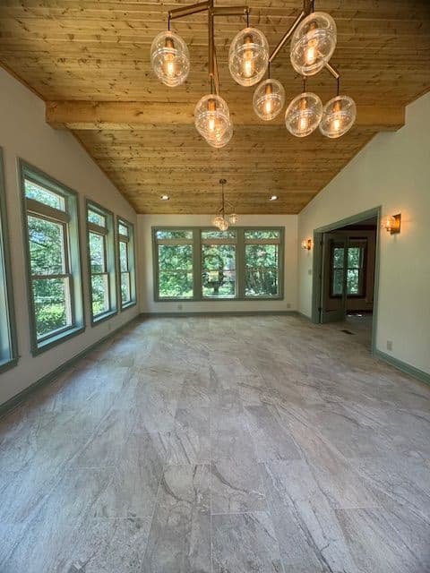 Spacious living room with wood ceiling, pendant lighting, and large windows showing greenery outside.