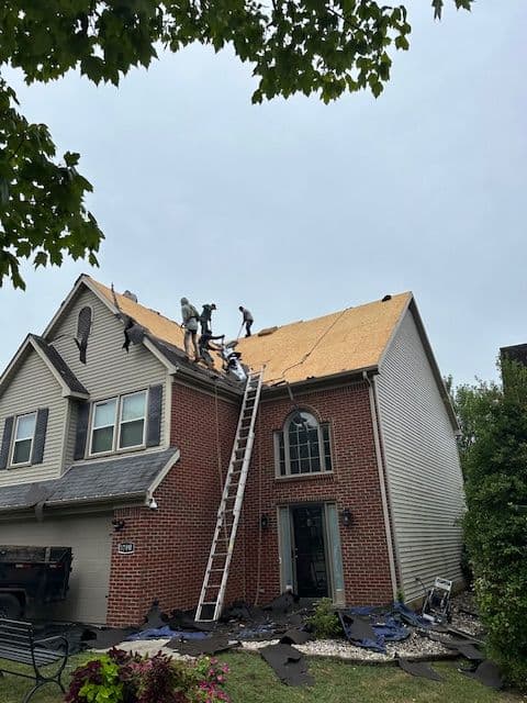 Roof replacement in progress with workers and ladder on a suburban house.