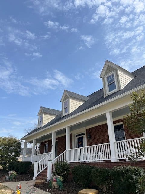 Charming brick house with a porch and gable roof under a blue sky.