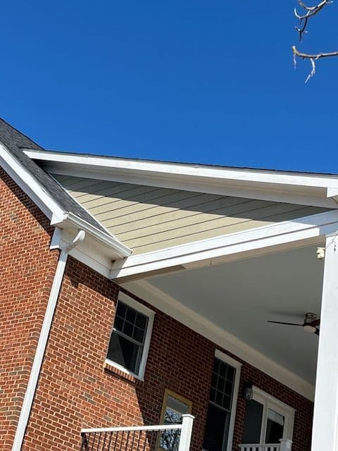 Close-up of a residential home's gabled roof under a clear blue sky, showcasing brick and siding details.