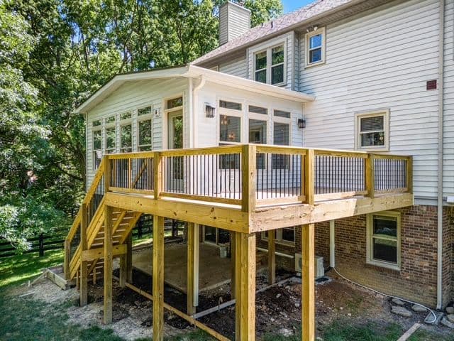 Elevated wooden deck with a sunroom, surrounded by trees in a residential backyard.