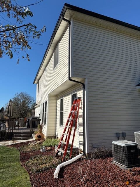 Two-story home exterior with a ladder, landscaping, and an air conditioning unit.