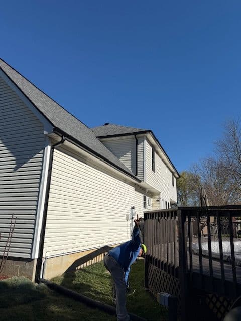 Person cleaning a roof with a clear blue sky in the background, residential house setting.