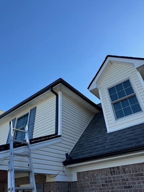 Home exterior with a ladder, showcasing new siding and roof details under a clear blue sky.