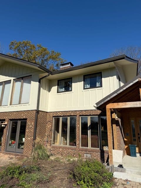 Modern two-story house with brick and siding, featuring large windows and blue sky backdrop.