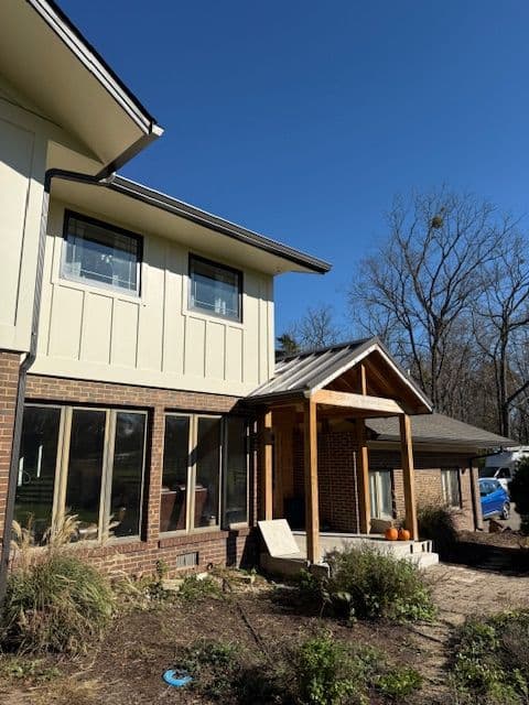 Modern home exterior with a wooden porch, large windows, and landscaped garden under clear blue sky.