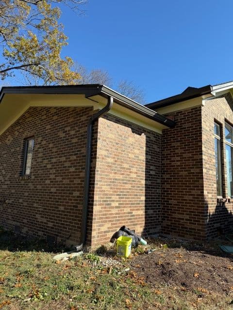 Corner view of a brick house with new gutters and sunny blue sky in the background.