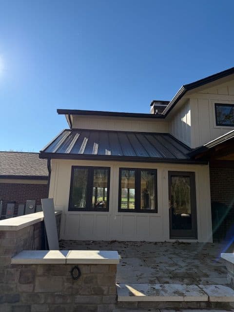 Modern home exterior with metal roof and large windows under a clear blue sky.