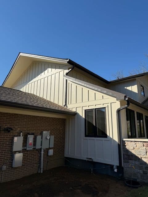 Modern home exterior featuring a combination of brick and vertical siding under a clear blue sky.