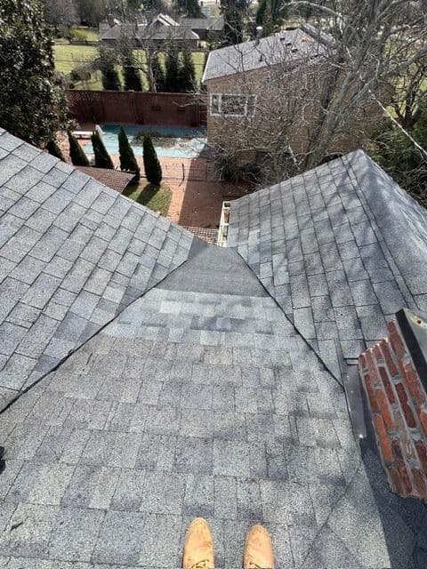 View from a rooftop showing shingles and a backyard with a pool and landscaped yard.
