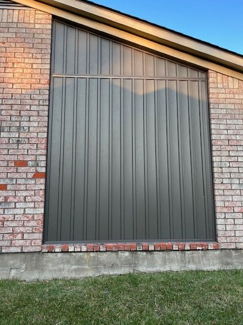 Exterior of a home featuring a vertical panel design on a brick wall with grass below.