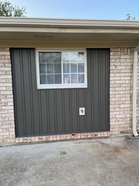 Exterior image of a brick house featuring a window and pet door on a gray panel wall.
