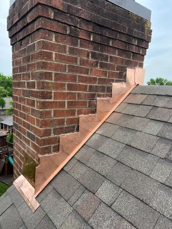 Copper chimney flashing on a brick chimney with shingles visible on the roof.