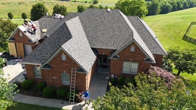 House with new roofing installation, surrounded by greenery and a worker on a ladder.