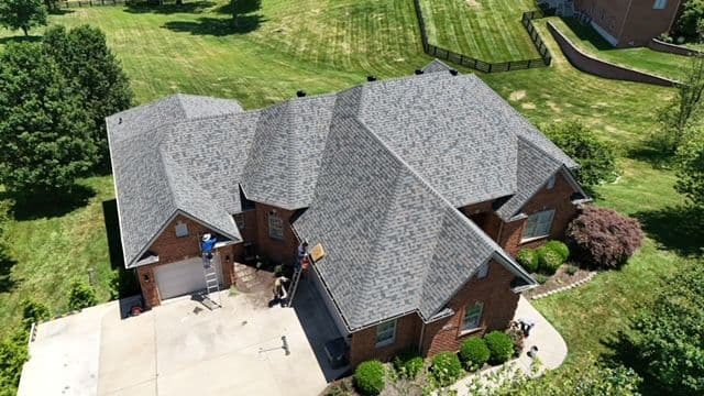 Aerial view of a brick house with a new gray shingle roof and manicured lawns.