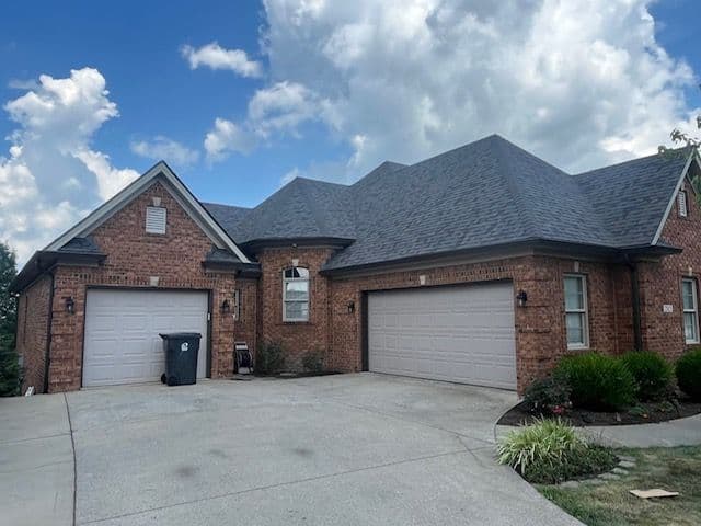 Brick house with dark gray roof and double garage on a sunny day with fluffy clouds.