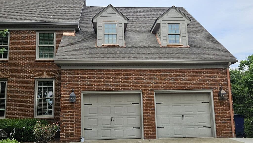 Brick house exterior featuring two dormer windows and a double garage with light fixtures.