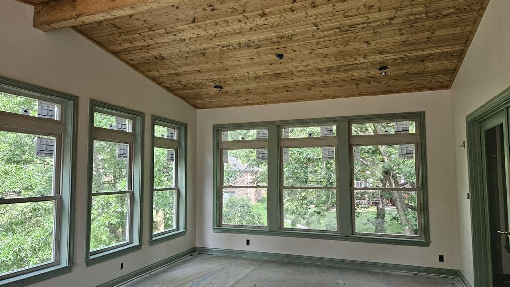 Spacious room with wooden ceiling and large windows overlooking greenery.