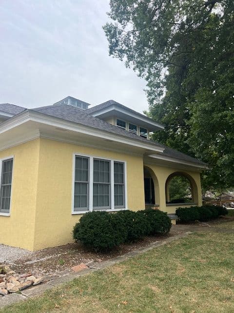 Yellow house with large windows, landscaped front yard, and arched entryway.