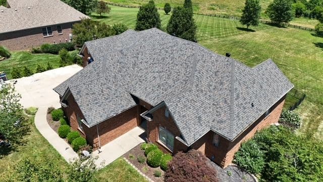 Aerial view of a large brick house with a grey shingle roof and landscaped yard.