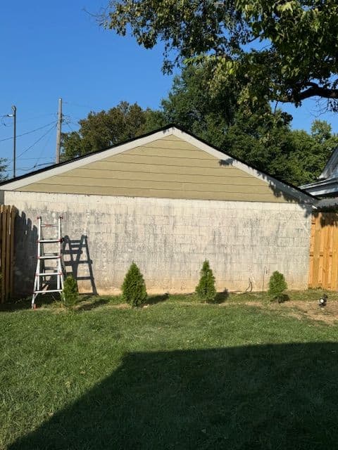 Backyard view featuring a shed, ladder, and newly planted shrubs against a grassy lawn.