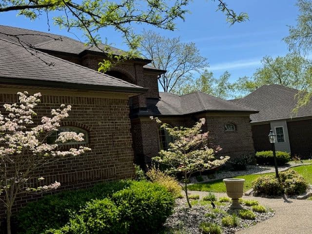 Exterior view of a brick house surrounded by blooming trees and lush landscaping on a sunny day.