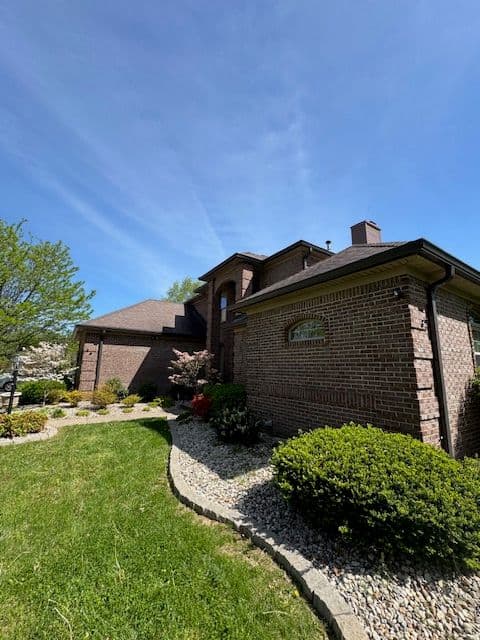 Brick house exterior with landscaped yard, blue sky, and greenery. Ideal for outdoor scenery.