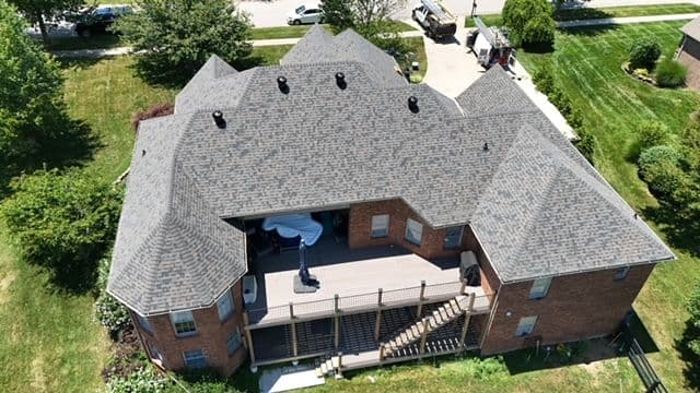 Aerial view of a large brick house with a spacious deck and lush green yard.