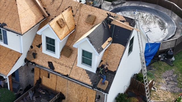 Roof being repaired after damage, showing tools, ladders, and work in progress.