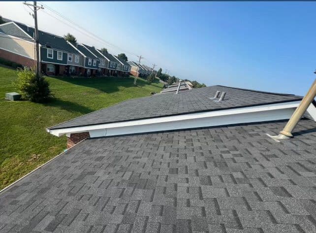 View of asphalt shingle roofs on residential buildings with green lawn and clear blue sky.