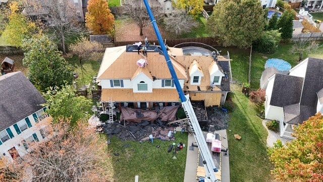 Aerial view of a house with ongoing roof replacement and construction equipment on site.