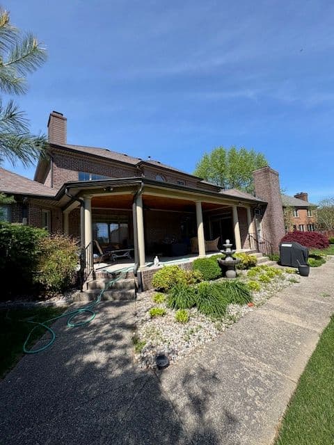 Brick home exterior with covered porch, landscaped garden, and clear blue sky.