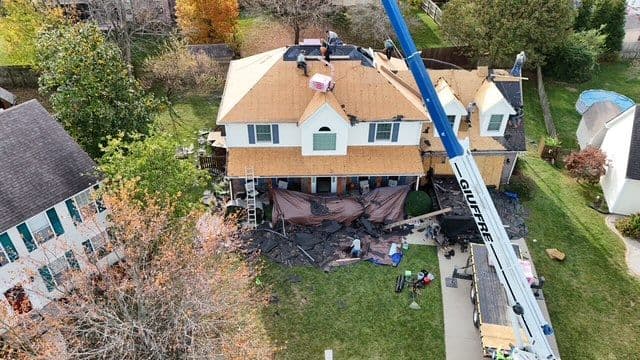 Roof renovation in progress on a suburban home with construction equipment and workers visible.