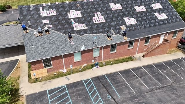 Roofing crew installing new shingles on a commercial building, with tools and materials visible.