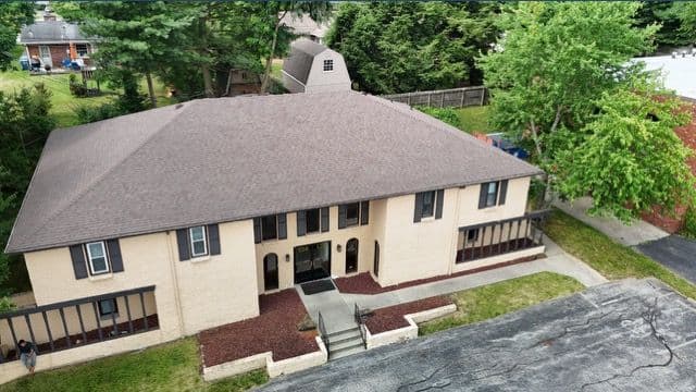 Aerial view of a beige multi-family building with landscaped grounds and parking area.
