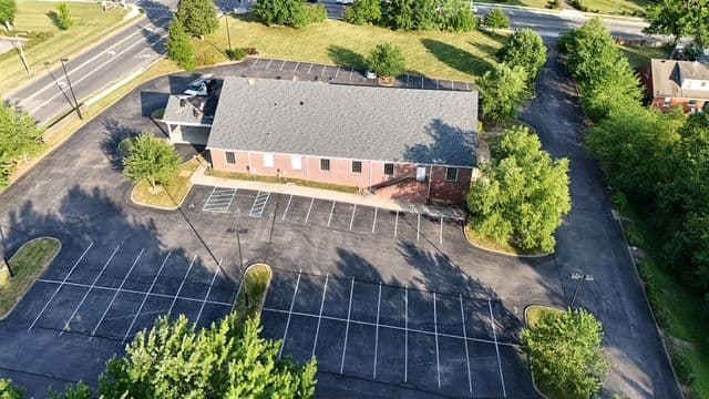 Aerial view of a large parking lot surrounding a brick building amidst green trees.