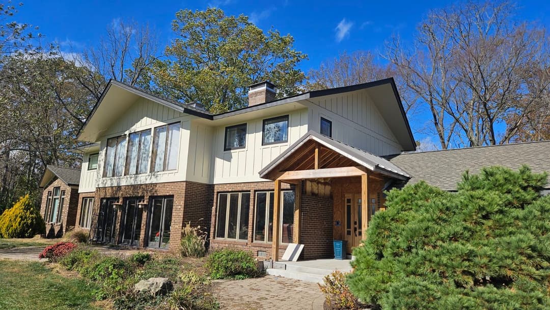 Modern two-story house with large windows, wooden entrance, and landscaped garden.