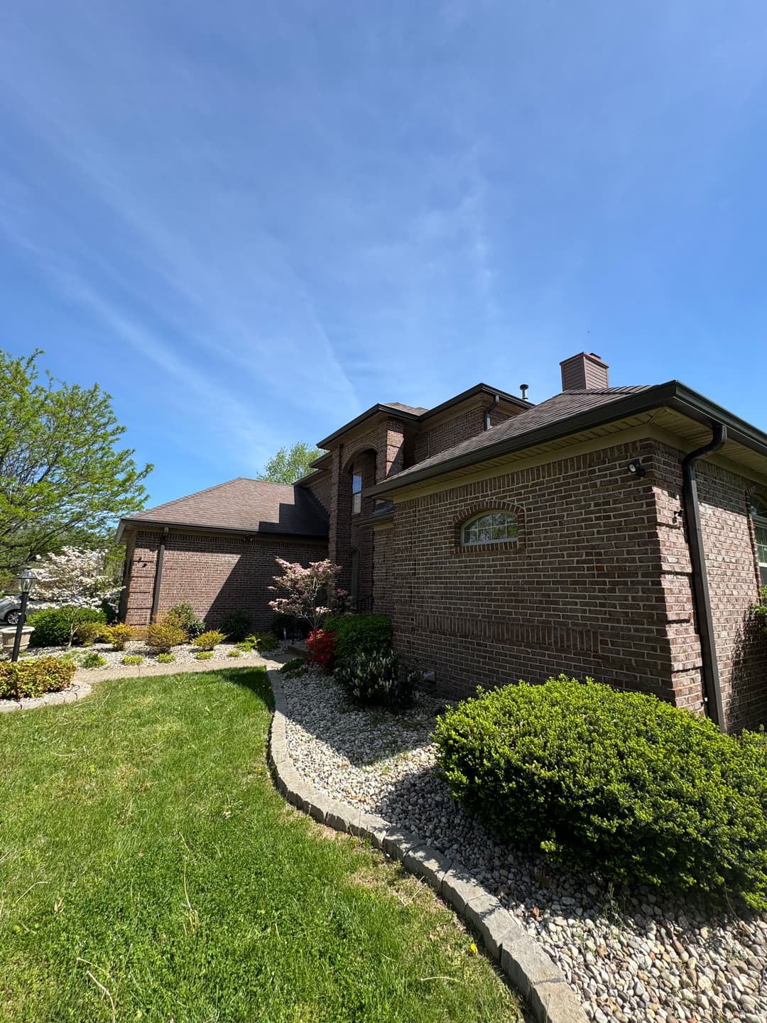 Two-story brick house with landscaped yard and clear blue sky, surrounded by greenery.