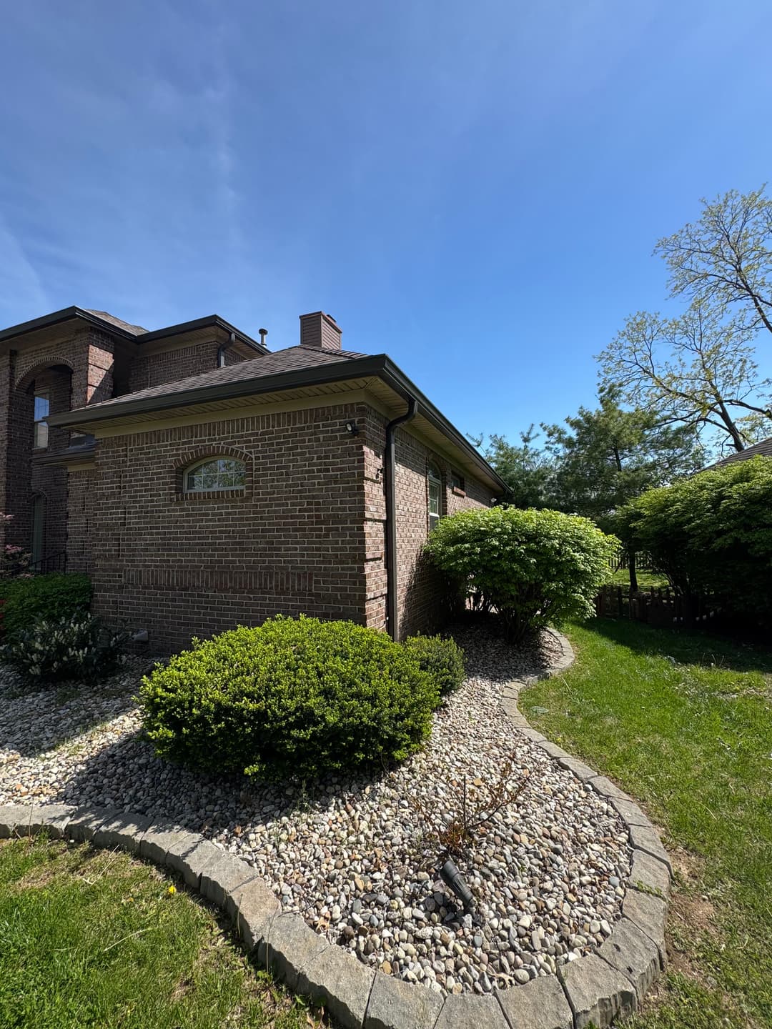 Brick house corner with landscaped rocks and shrubs under a clear blue sky.