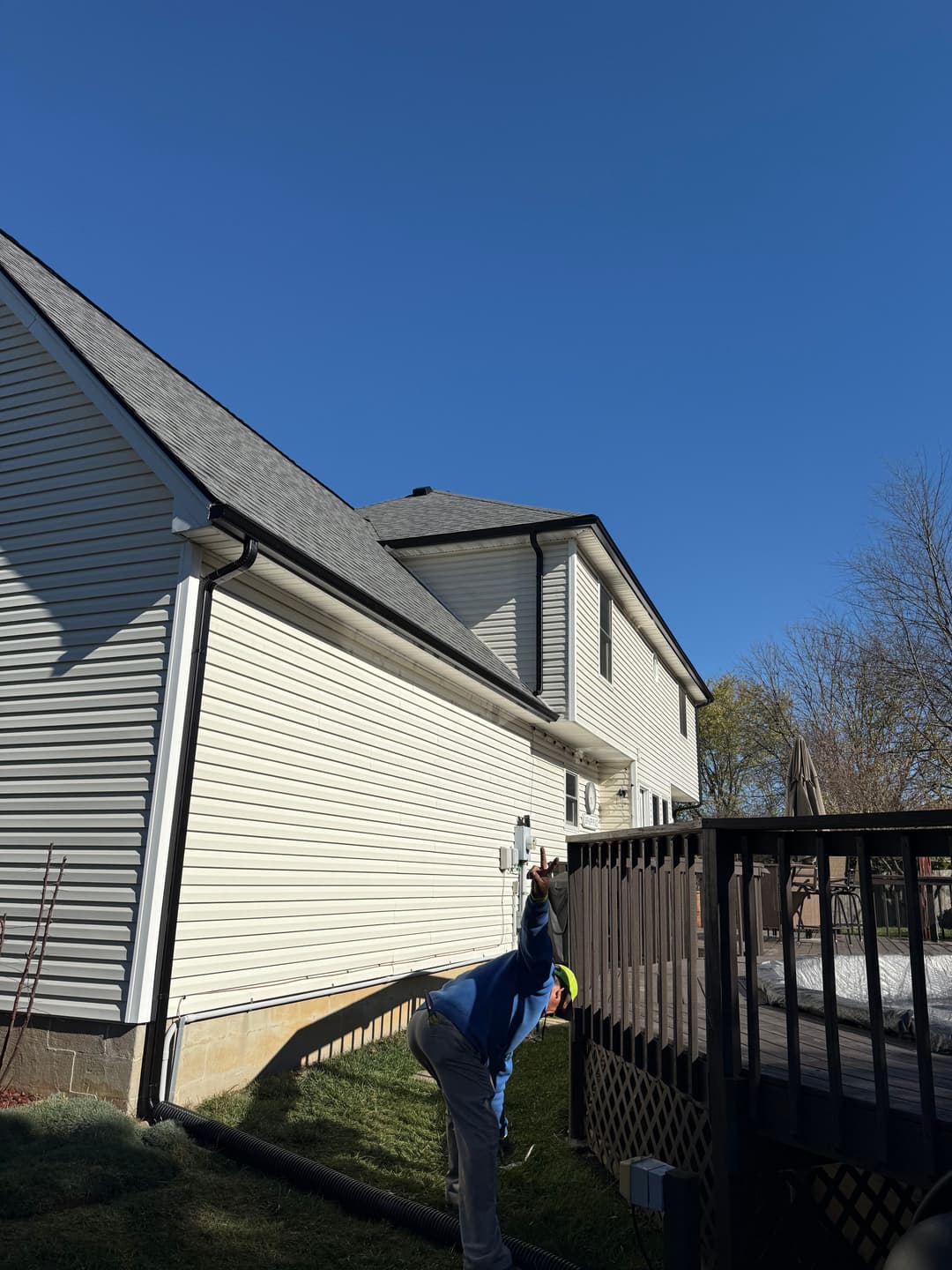Person pointing towards a clear blue sky near a house with a deck and green grass.
