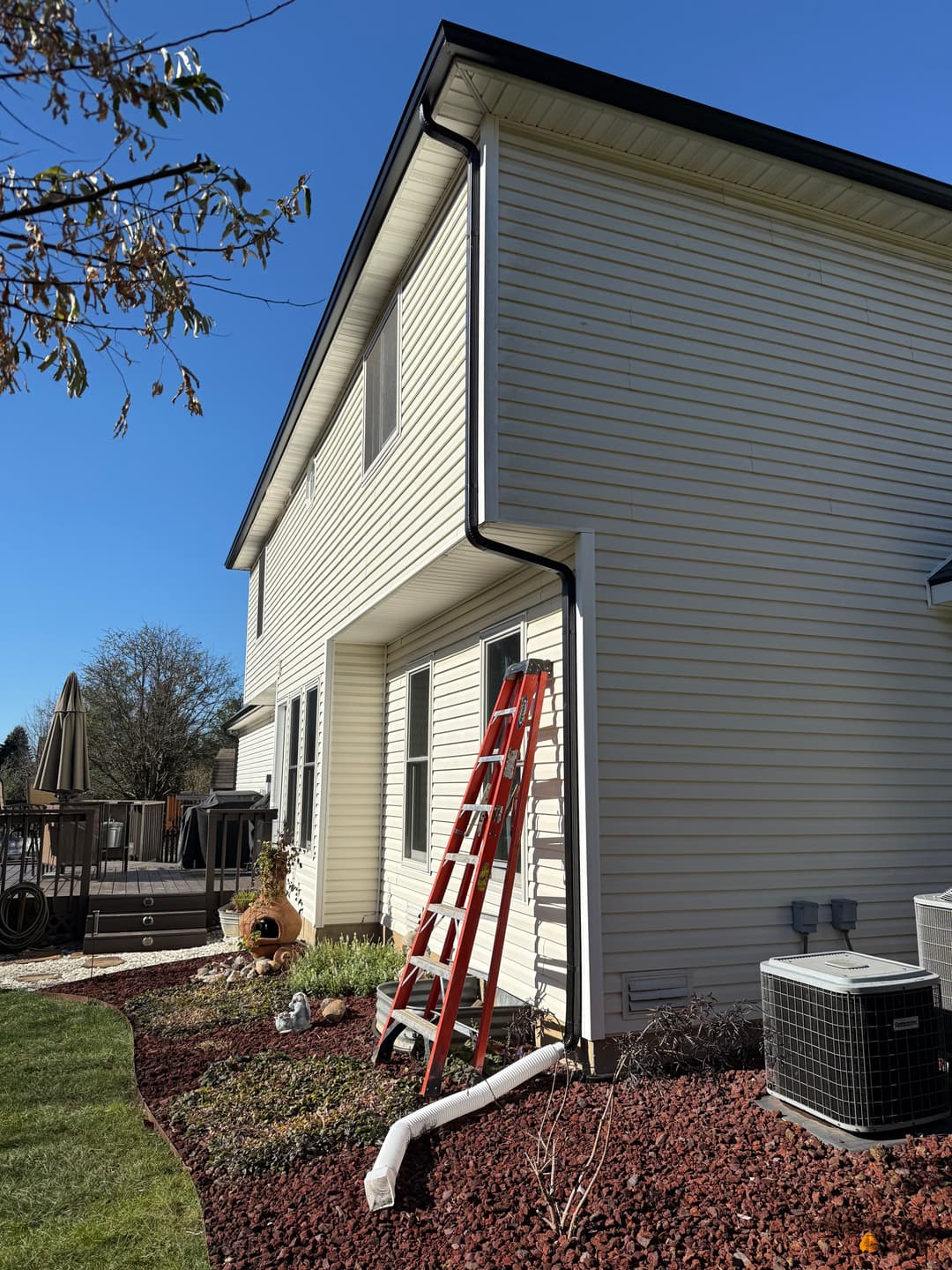 Residential house exterior with a red ladder, landscaping, and clear blue sky.