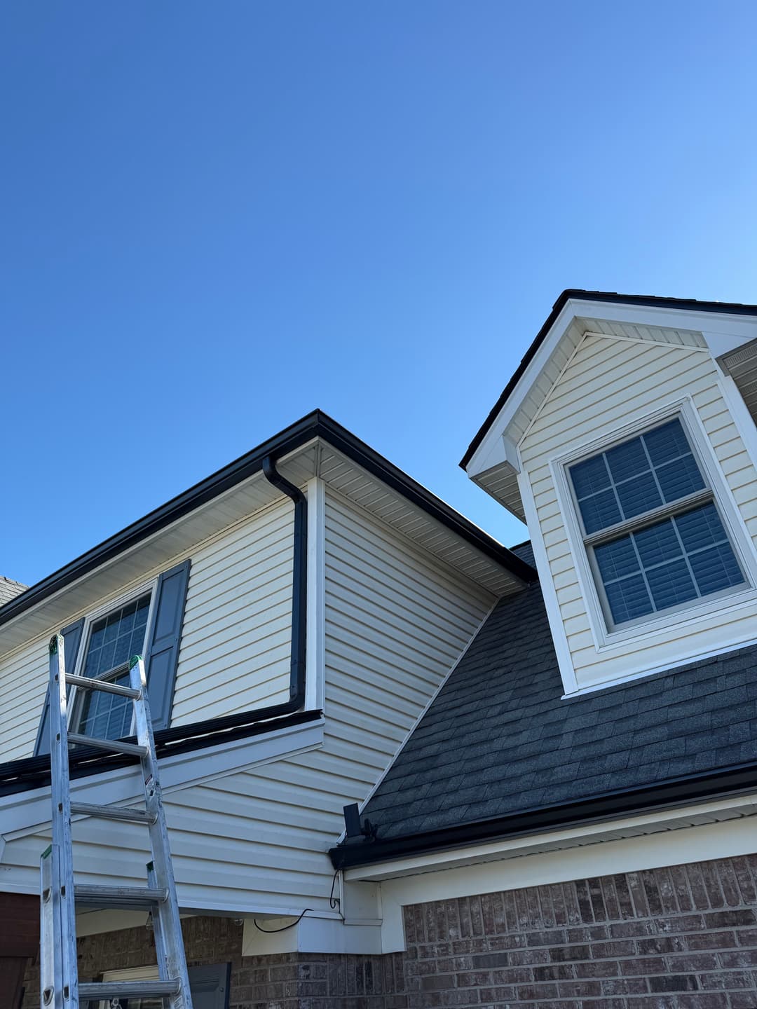 Residential exterior showing a ladder, vinyl siding, and clear blue sky.