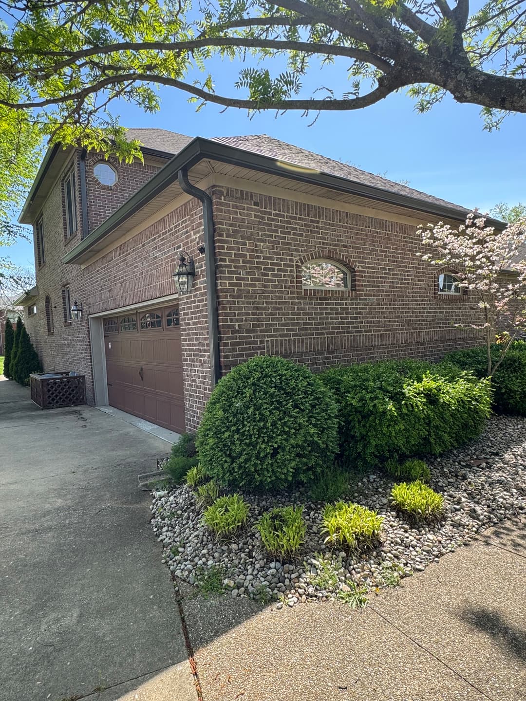 Brick house corner with landscaped garden and garage on sunny day.