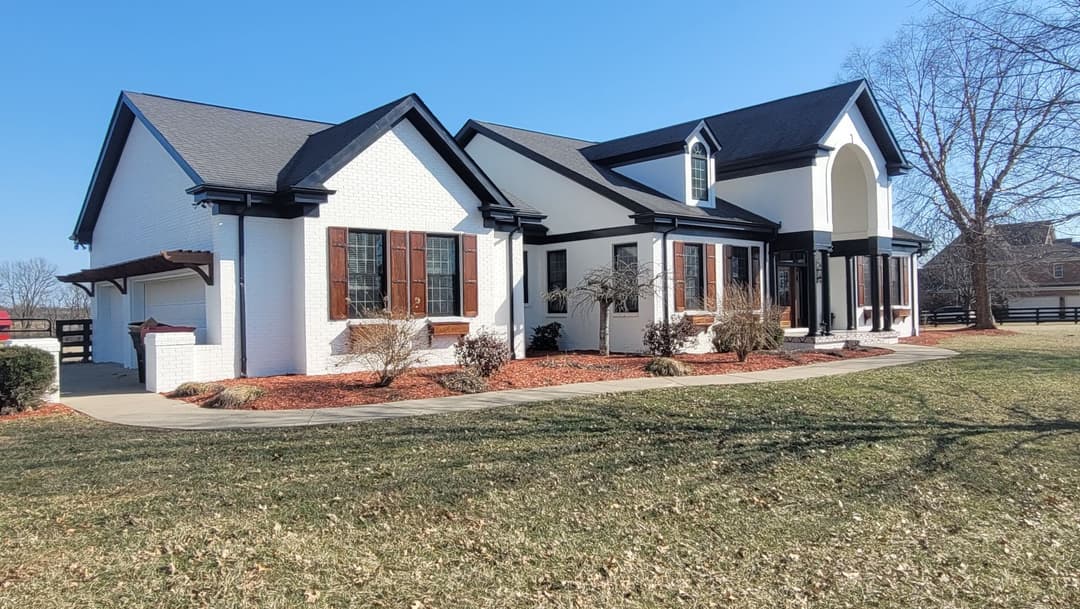 Modern house with white brick exterior, black roof, and landscaped yard on a sunny day.