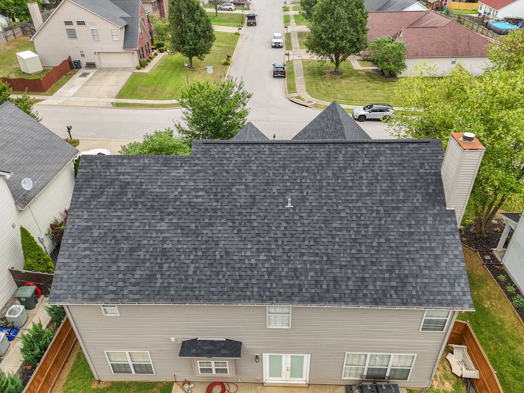 Aerial view of a residential home with a dark shingle roof and landscaped yard.