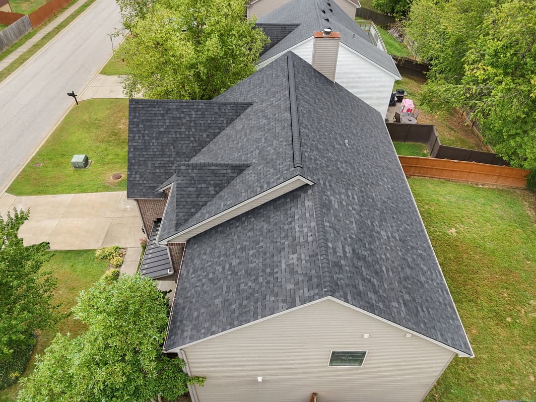 Aerial view of a modern house with a gray shingle roof and surrounding greenery.